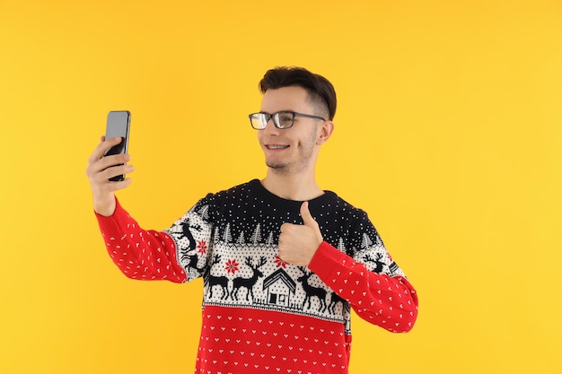 Guy in Christmas sweater with phone on yellow background