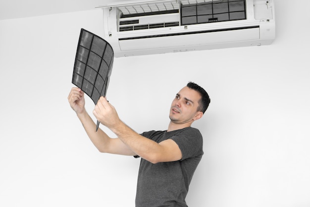 The guy cleans the filter of the home air conditioner from dust. The guy snayed a very dirty air conditioning filter. and examines it in his hands. Climate equipment care.