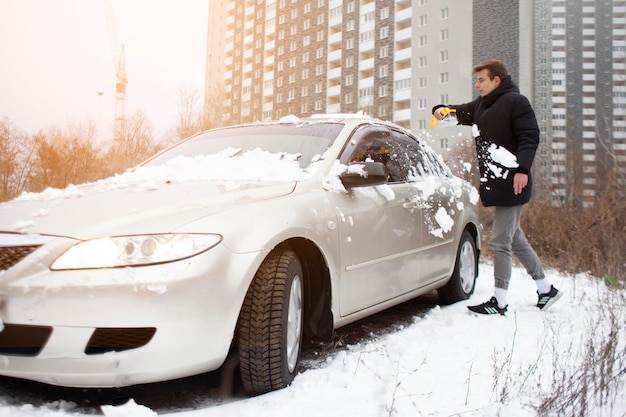 男は車からブラシで雪をきれいにします 男は冬に車の世話をします