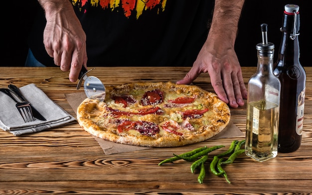 The guy cuts pizza on a wooden table