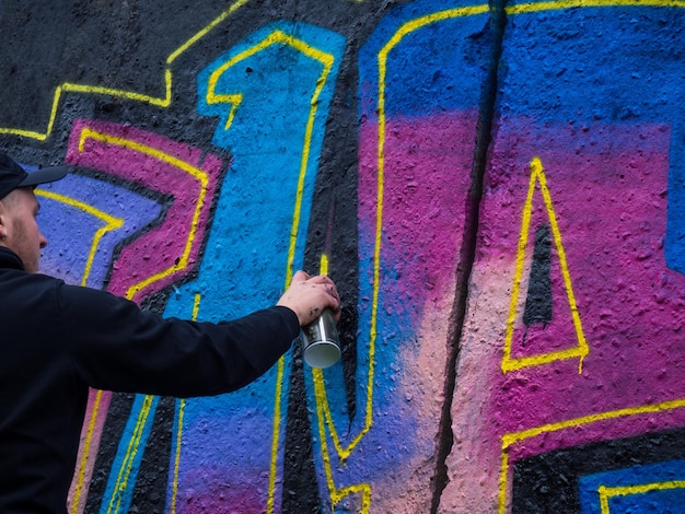 The guy draws a bright colorful graffiti on a black wall