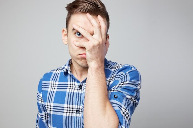 guy dressed in a plaid shirt and jeans closes his face with his hand