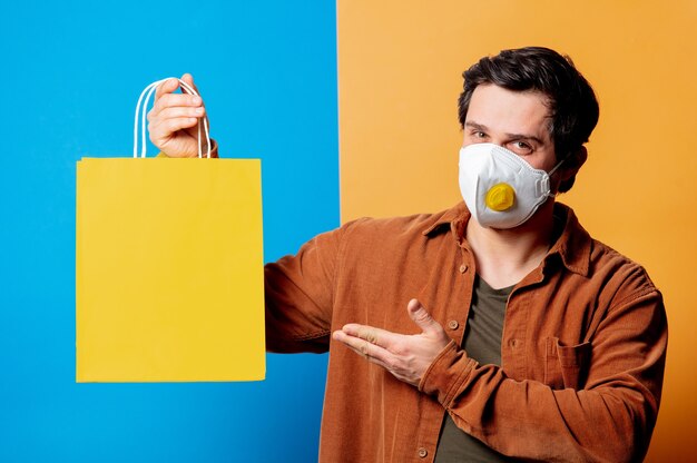 Guy in FFP2 face mask hold shopping bag on yellow and blue backgrounds