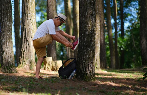 A guy fixing his shoe lace on a tree while hiking across pine woods