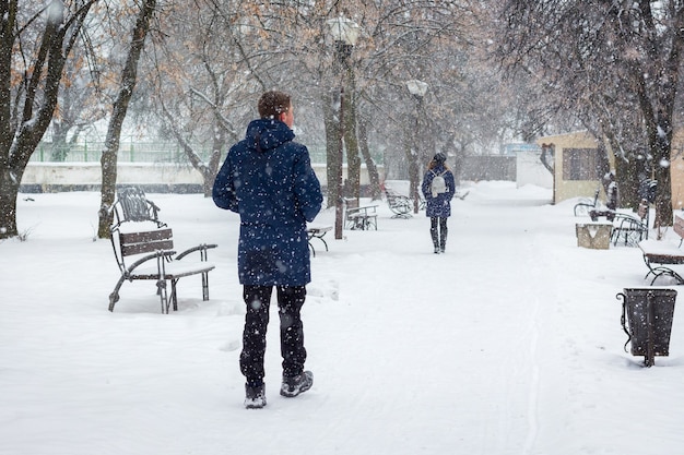 Il ragazzo segue la ragazza nel parco invernale durante la nevicata_