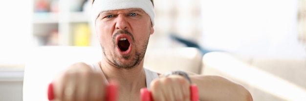 Guy fulfills strokes with dumbbells in his hands. Physical exercises during self-isolation. Home exercises after watching home fitness videos. Strength and perseverance towards ideal figure