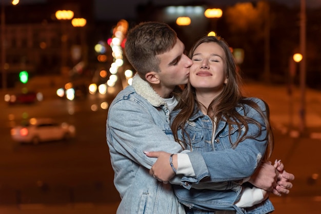 男は夜の街の背景に優しく抱擁と彼のガールフレンドにキスします