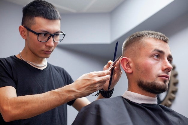 Guy get a haircut in a barbershop a young Kazakh barber cuts manually with scissors