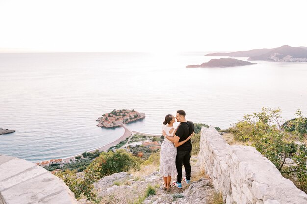 Foto ragazzo e ragazza quasi baciarsi su una montagna con vista sull'isola di sveti stefan montenegro vista posteriore