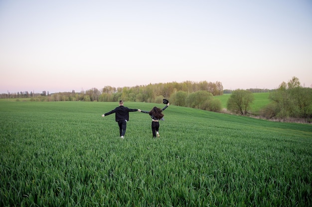 A guy and a girl are running in a green field with their arms outstretched