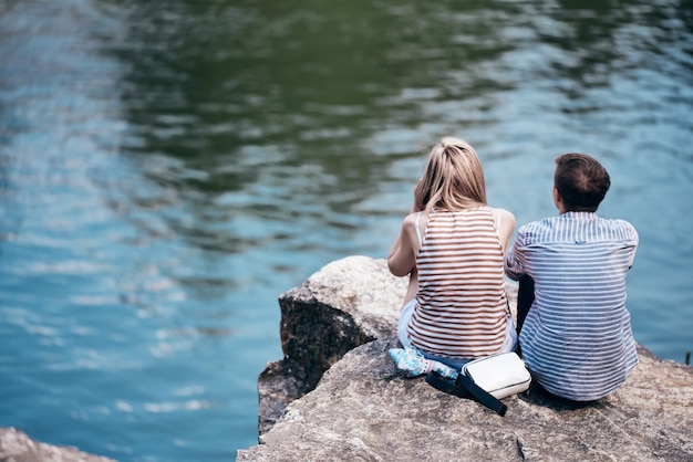 男と女は川の上の崖に座って、正面を向いています。背面図