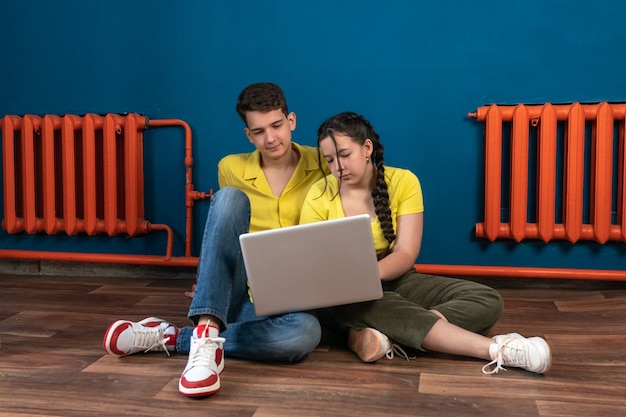 a guy and a girl are sitting on the floor with a laptop in their hands and watching a video