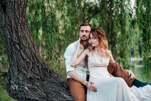 Парень и девушка сидят вместе на кривом дереве на крутом берегу дикой реки