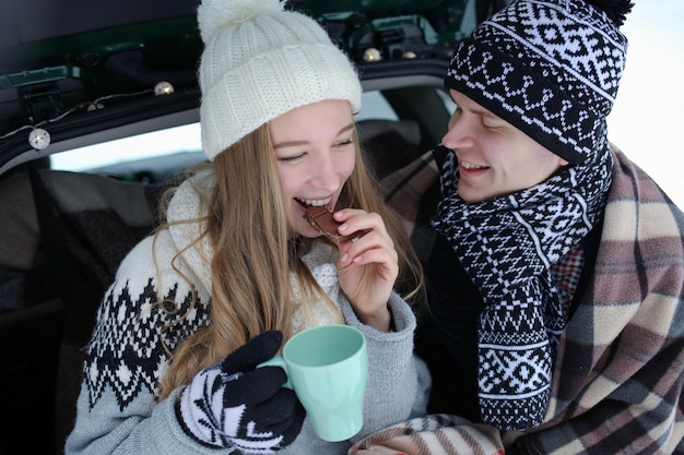 a guy and a girl are sitting in the trunk of a car, in a blanket with a cup of tea