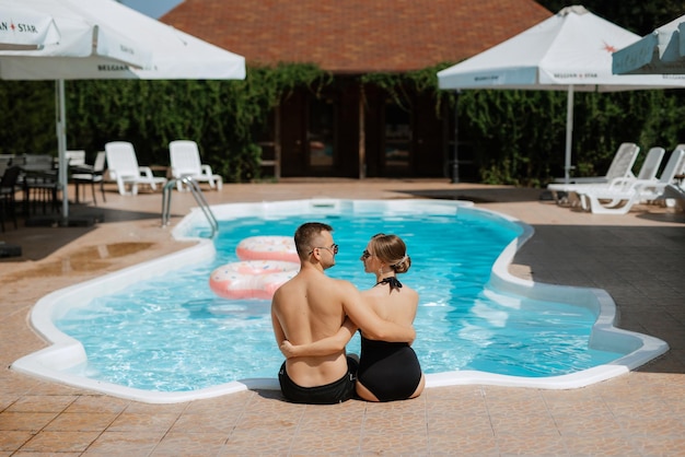 Foto ragazzo e una ragazza in costume da bagno si rilassano vicino alla piscina blu