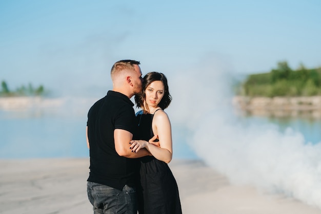 Guy and a girl in black clothes hug inside a white smoke