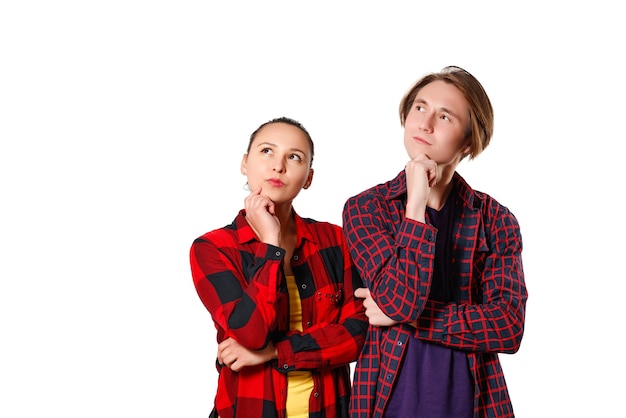 A guy and a girl in casual clothes, checkered shirts are standing and looking thoughtfully towards the copyspace. isolated on white background