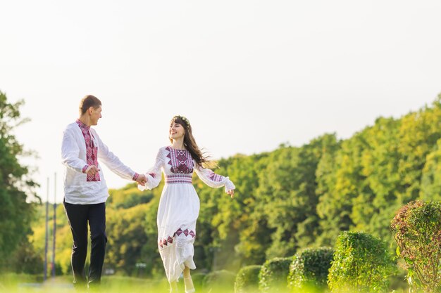 Guy and girl in embroidered clothes holding hands and running in the park have fun nature