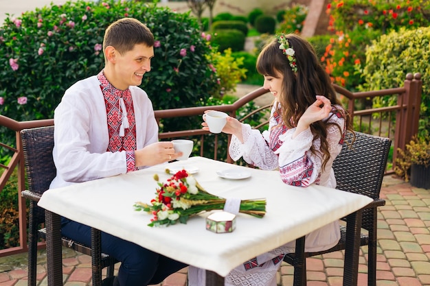 Guy and girl in embroidered clothes sitting in cafe and drinking hot coffee