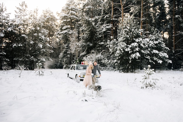 Un ragazzo e una ragazza si preparano per natale, portando a spasso il cane husky su uno sfondo di auto d'epoca, sul tetto e regali nella foresta innevata d'inverno