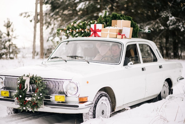 A guy and a girl go in a retro car decorated with a Christmas tree