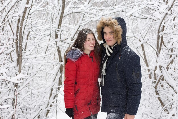 男と女は冬の森で休む雪の中で夫と妻ウィンターパークを歩く若いカップル