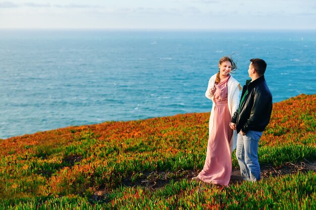 Guy and girl hold hands and smile on the shore of the ocean.