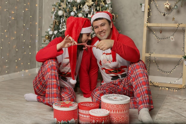 у елки сидят парень и девушка в пижаме и шапке Деда Мороза