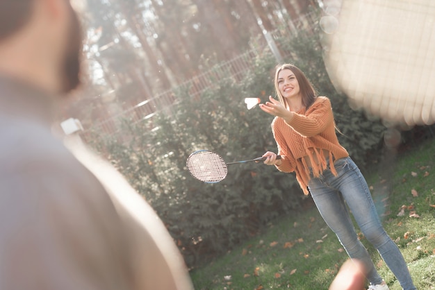 A guy and a girl play badminton during a picnic with friends.