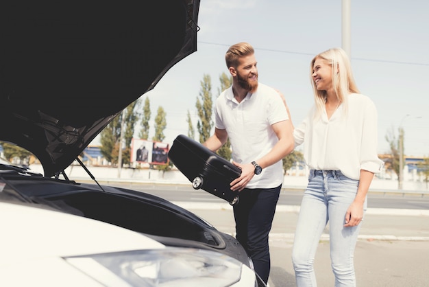 Guy and a girl put luggage in trunk of their electric car 