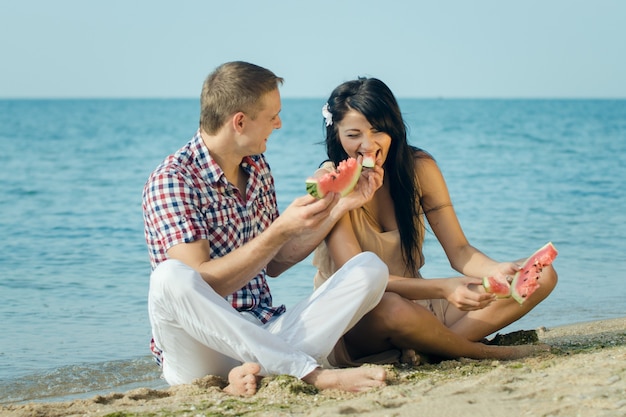 Guy and a girl on the seashore eating a ripe red watermelon