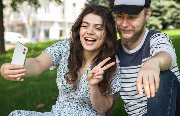 A guy and a girl take a selfie sitting on the grass in the park