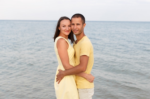 Парень и девушка в желтой одежде стоят в объятиях на пляже