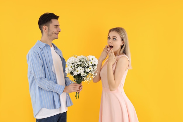 A guy gives a bouquet to a girl on yellow background