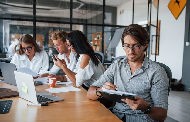 Guy in glasses in front of his employees. Young business people in formal clothes working in the office.