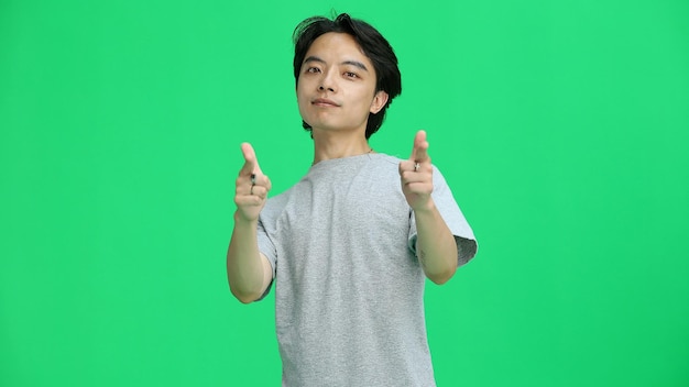 A guy in a gray Tshirt on a green background closeup pointing forward