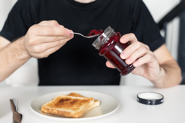 男はジャム付きのトーストで朝食をとります。