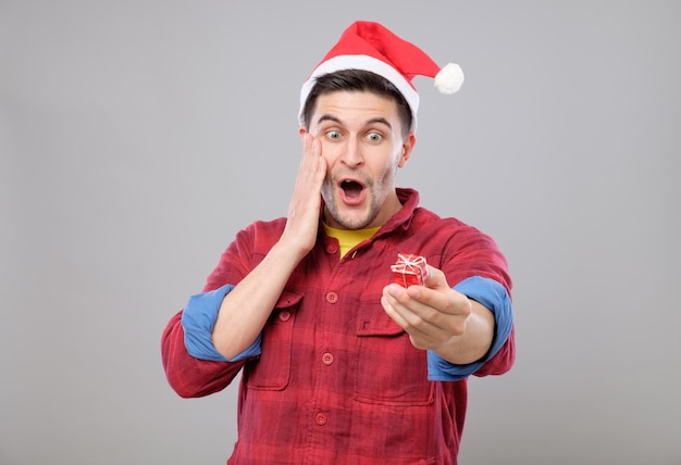 Guy holding a gift and emotionally happy Christmas isolated on gray background