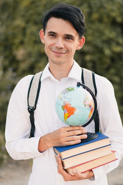 Ragazzo in possesso di una pila di libri con un globo