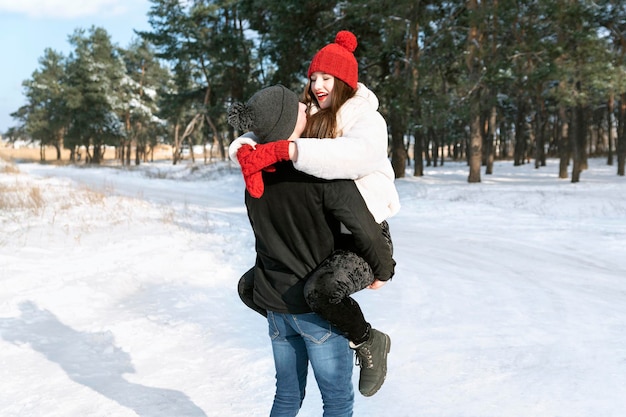 Guy holds her girlfriend in his arms on snowy forest background Walks through winter forest and fools around