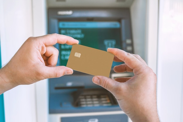 The guy holds in his hand a bank card in front of the ATM.