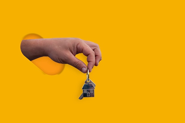 가이는 노란색 배경에 격리된 손에 집 열쇠를 들고 있습니다. 새 집을 사는 주제에 대한 개념입니다.