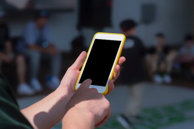 The guy holds a mock-up of a smartphone in his hand against the background of the children's dance championship.