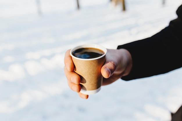 男は雪の森で彼の手にコーヒーの紙コップを持っています。