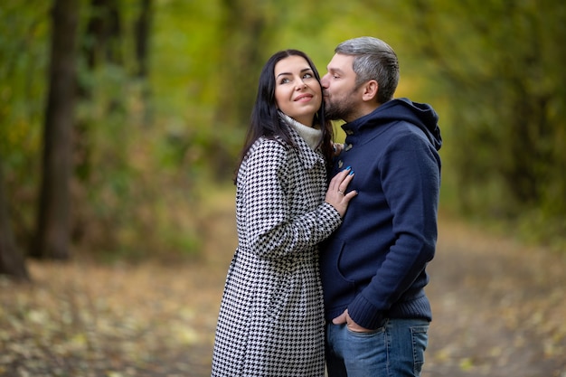 한 남자가 가을 공원에 서 있는 소녀를 안고 키스합니다. 고품질 사진