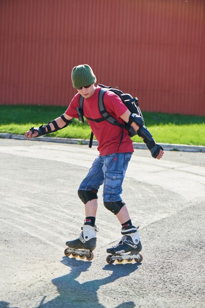 The guy is going backwards on roller skates on an asphalt track against the red wall