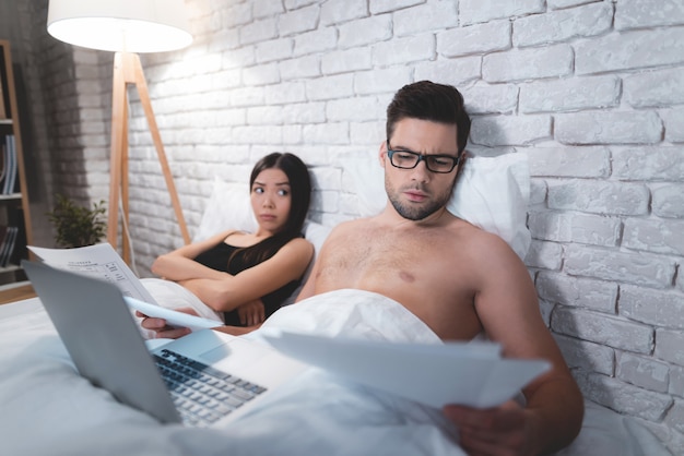 A guy is lying in bed and working on a laptop.