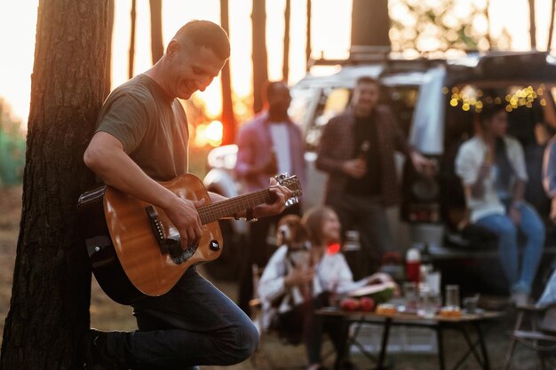 Foto un tizio sta suonando la chitarra acustica un gruppo di amici si sta divertendo insieme nella foresta