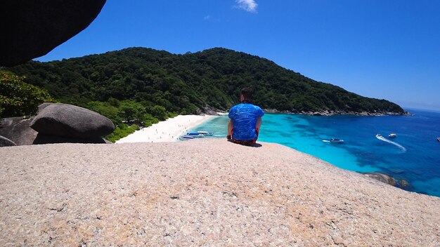 The guy is sitting on a rock and looking at lagoon