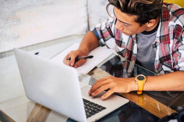 Guy is studyng or doing homework with his laptop or computer on the table - focused - guy boy black and blonde hair looking his homework